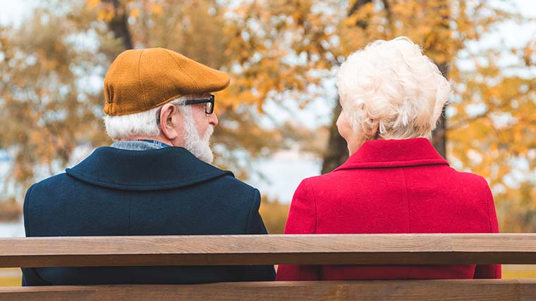 Senior man och kvinna sitter ute och samtalar på en bänk. 