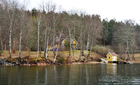 Ett foto som visar ett gult trähus och ett litet badhus vid bryggan.