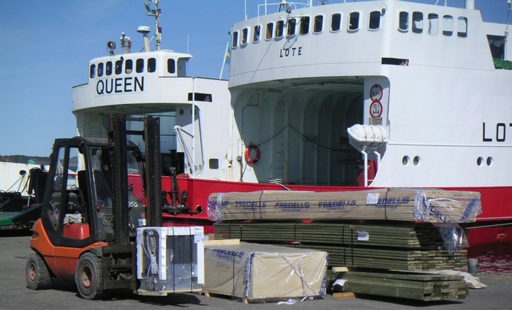 En truck plockar upp last och två fartyg ligger vid kajen.