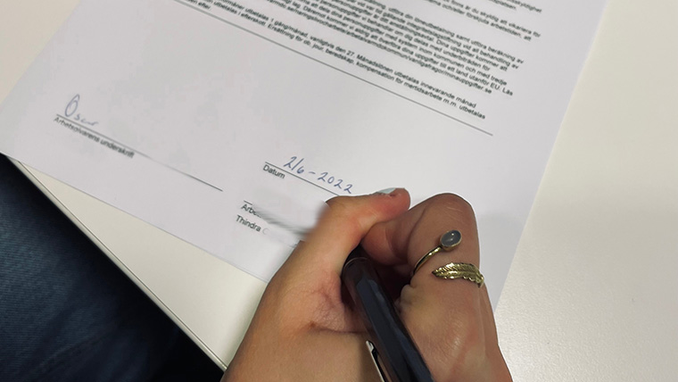 En hand håller i en penna och skriver under ett papper