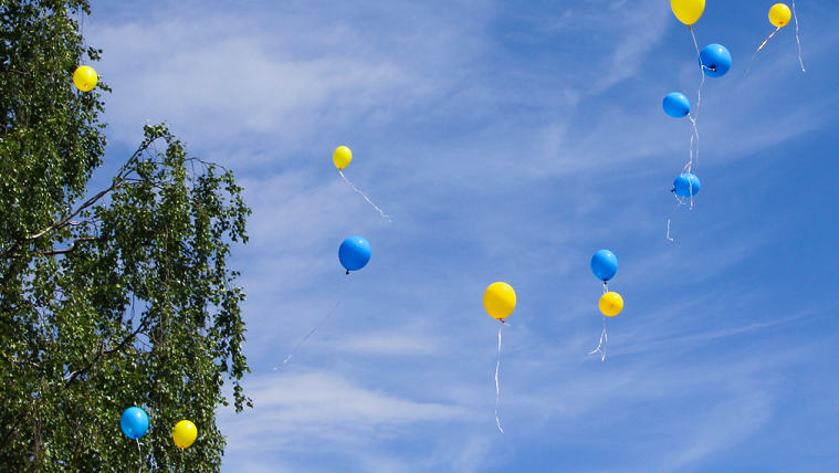 Ballonger i gult och blått svävar upp mot sommarhimmel. 