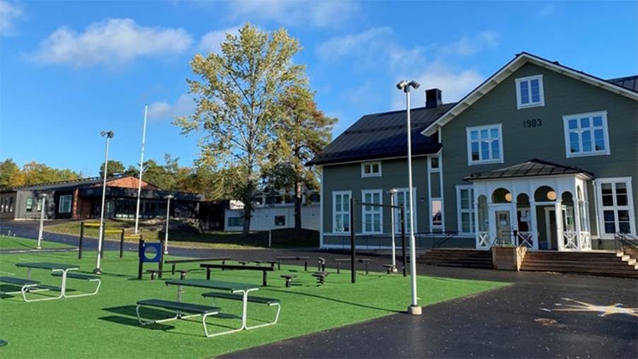 Bild på skolgården. En stor grön plan syns omgiven av hus.