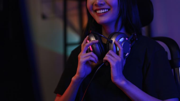 En leende tjej med gaming-hörlurar runt halsen. 