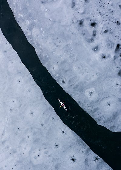 En kanotist paddlar genom fruset, snölandskap.